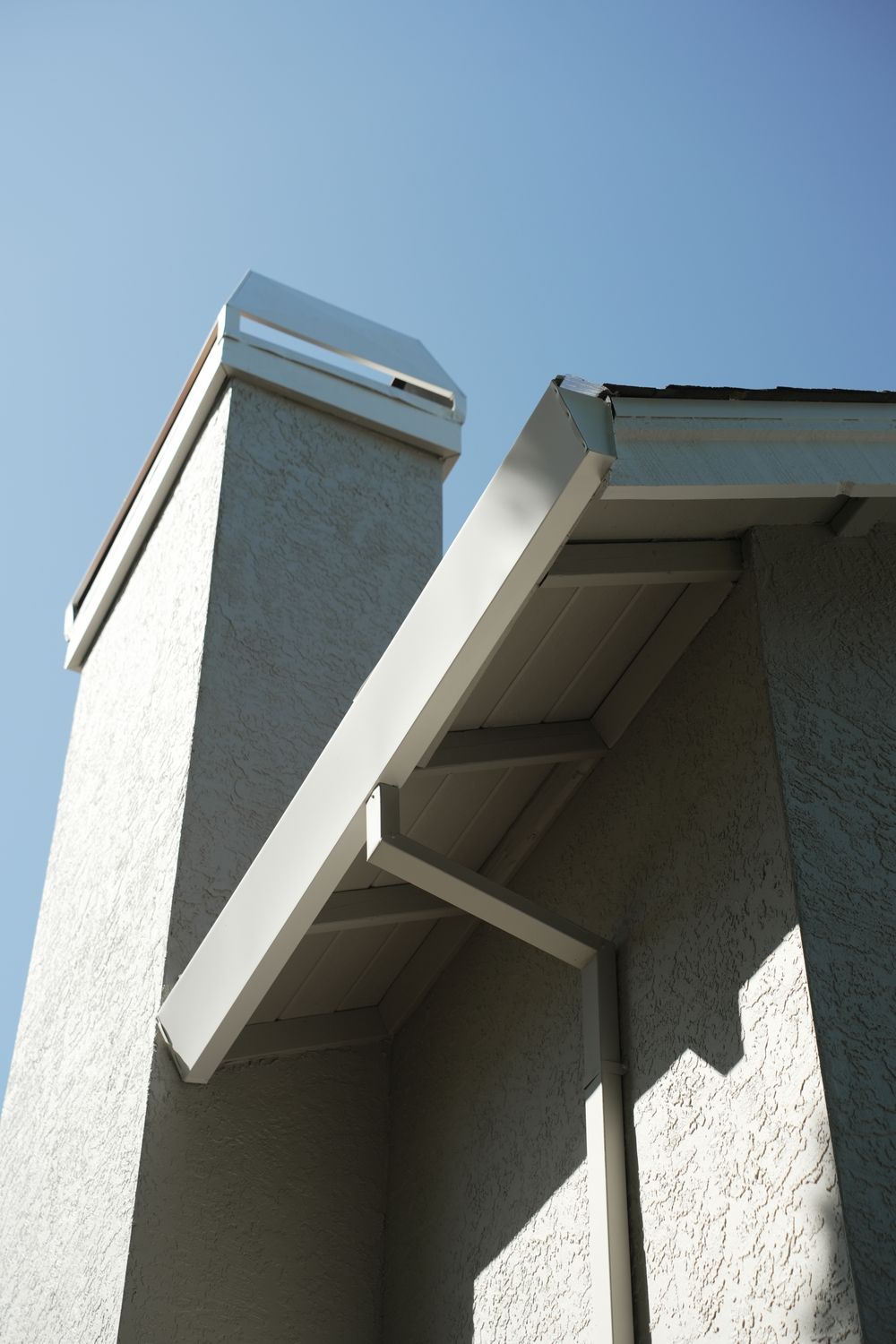 Chimney and eave on the finished exterior, with white fascia and gutter against a blue sky.