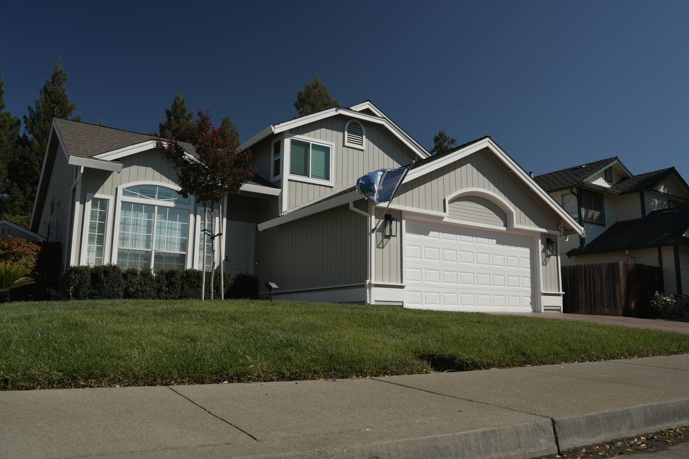 Wide view of the finished front of the home, with light siding, white trim and a white garage door.