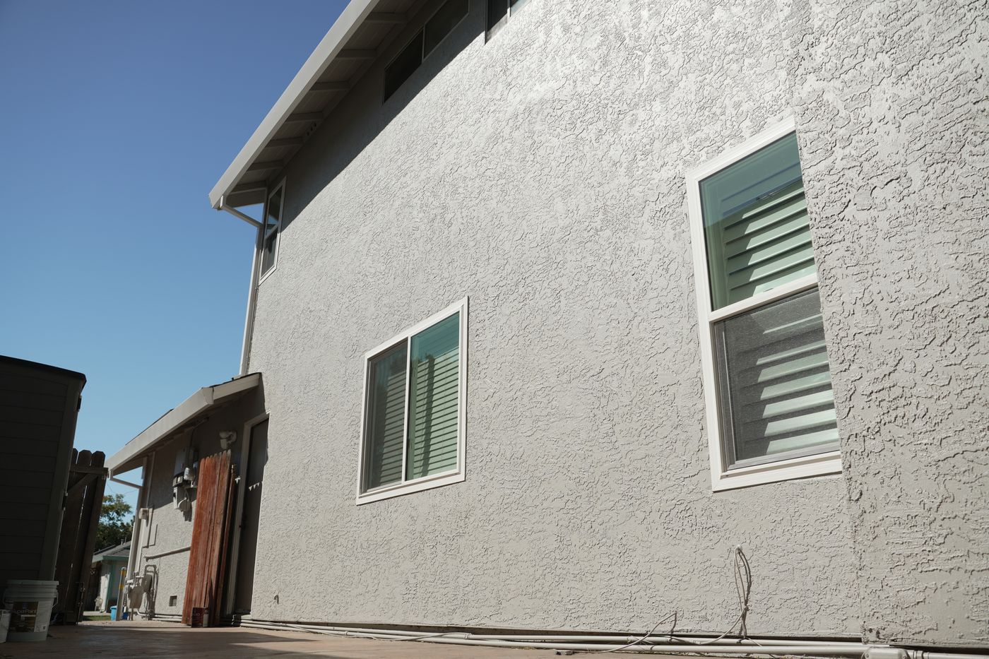 Finished textured side wall with white-trimmed windows under a clear blue sky.