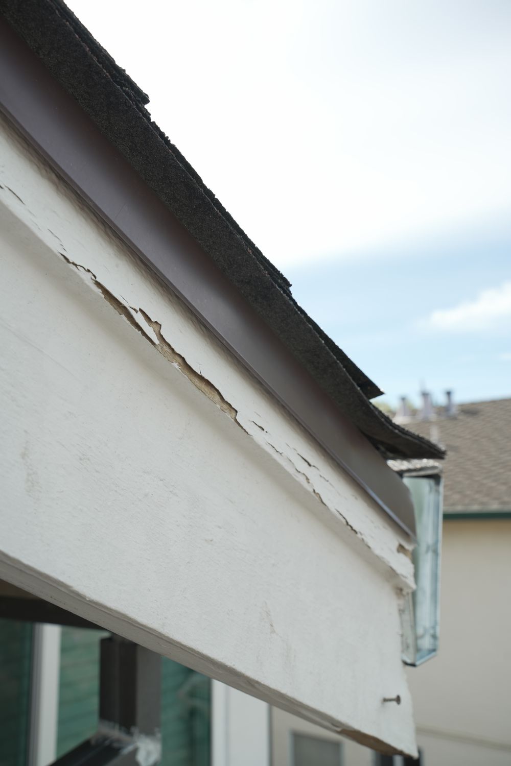 Close-up of cracked and peeling paint along the edge of a painted fascia board beneath the roofline.
