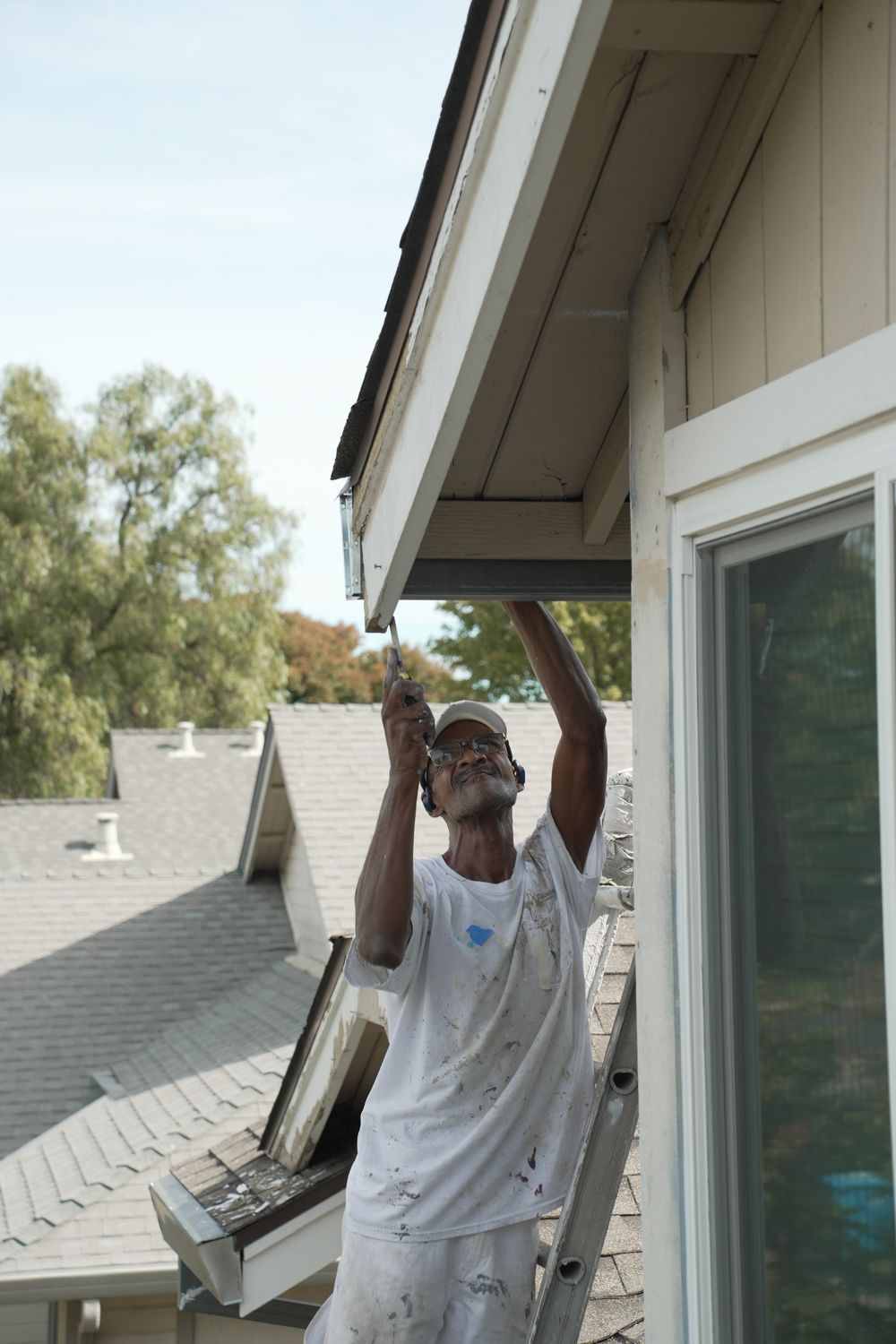 Milestone crew member using a hand tool to scrape paint from exterior trim beneath an eave.
