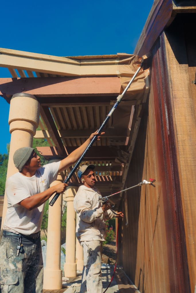 Milestone Painting crew staining pergola and wood siding on estate