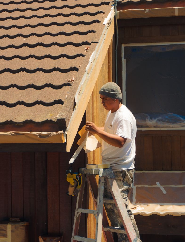 Painter on ladder masking and prepping wood siding before staining — Milestone Painting
