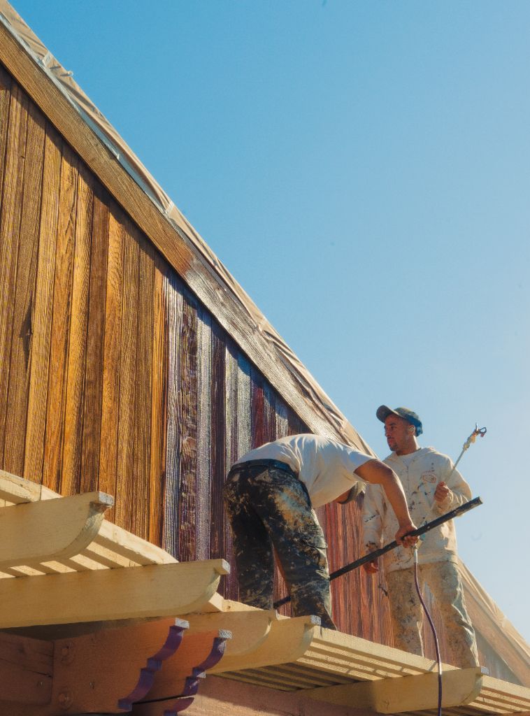 Painter using airless sprayer to apply stain to wood siding — Milestone Painting NorCal